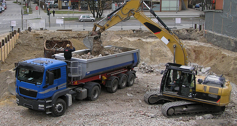 Ein LKW wird auf einer Baustelle von einem Bagger beladen.