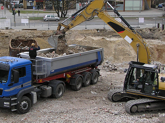 Ein LKW wird auf einer Baustelle von einem Bagger beladen.